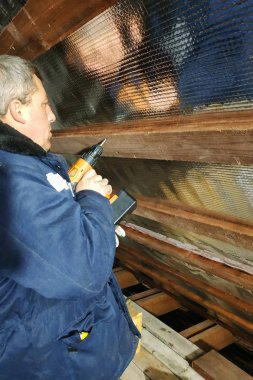 Sihirbaz Akülü matkap kullanır ve sabitleyen vidayı folyo film ve mineral yün Evin çatısı iyileşmek için tutun panoları vida