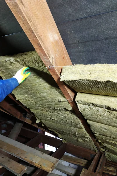 A man installs a thermal insulation layer of a thermal roof - using panels of mineral wool, mounting it between the beams of the roof of the house for warming from the cold