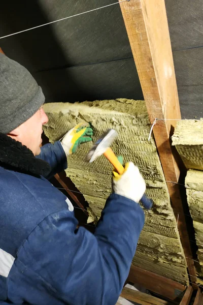 En man installerar ett värmeisolerande lager av termiska tak - med hjälp av paneler av mineralull, montera den mellan balkar av taket av huset för uppvärmningen från kylan — Stockfoto