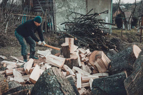 Um homem forte colhe lenha para o inverno no quintal da casa cortando a árvore de grama grande e resistente — Fotografia de Stock