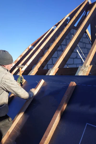 The master nails the bars, fixing this gidrorizer to the rafter, the blue sky appears on the background