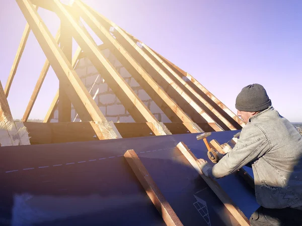 The master nails the bars, fixing this gidrorizer to the rafter, the blue sky appears on the background