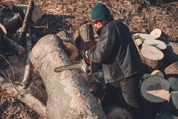 Menina rural jovem cortou uma motosserra de árvore em luvas, cozinhe lenha para o inverno — Fotografia de Stock