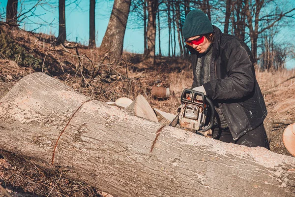 Menina rural jovem cortou uma motosserra de árvore em luvas, cozinhe lenha para o inverno — Fotografia de Stock