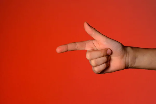 Mano humana con los dedos doblados, muestra un dedo índice que simboliza una pistola, aislada sobre un fondo rojo — Foto de Stock