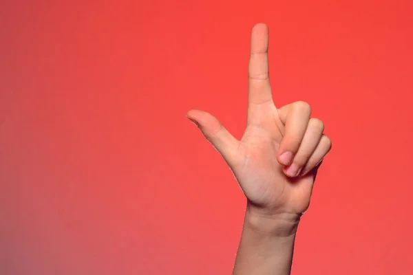 Mano humana con los dedos doblados, muestra un dedo índice que simboliza una pistola, aislada sobre un fondo rojo — Foto de Stock