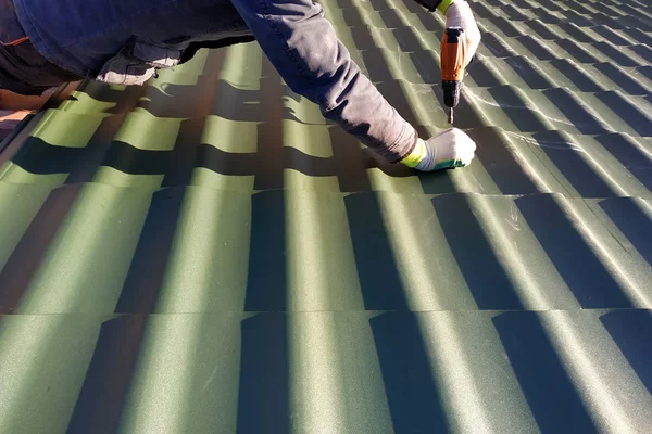 Професійний працівник працює над установкою даху з листів металевої плитки і свердлить гвинт дрилем — стокове фото