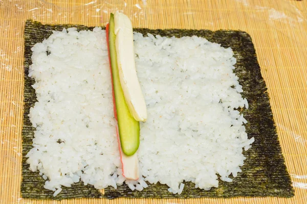 Des sushis maison. Les mains masculines préparent des petits pains avec riz, saumon, crabe, fromage, nori, concombre — Photo