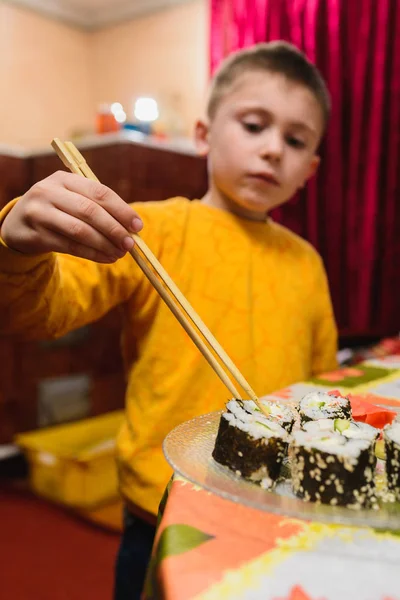 Der Teenager nimmt die Sushi-Rolle vom Teller zum Essen — Stockfoto