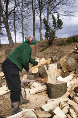 Yaşlı bir kadın baltayla odun parçalar, kış için odun hazırlar..