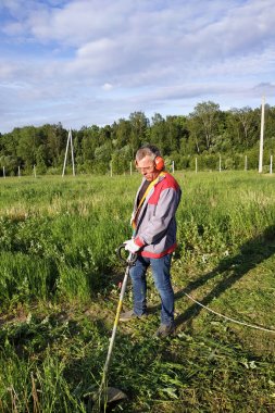 Kulaklık ve gözlük işçisi tarladaki çimleri biçiyor.