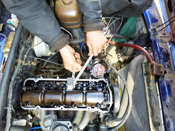 De kleppen met een auto-illuminator in de garage in een oude auto aanspannen. — Stockfoto