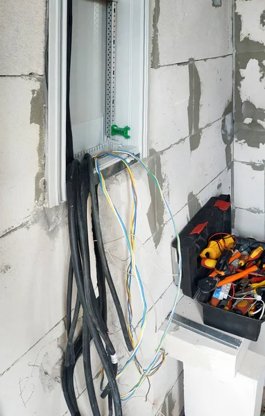На стене недавно построенного дома установлен новый электрический щит, видны кабели и инструменты . — стоковое фото