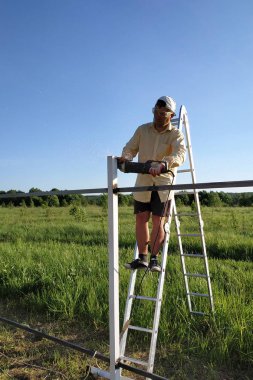 Ana merdivenüzerinde duran bir açı değirmeni ile çitin metal profilinin kalıntıları keser.