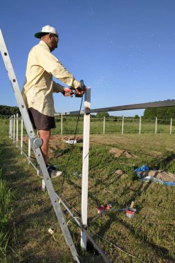 Ana merdivenüzerinde duran bir açı değirmeni ile çitin metal profilinin kalıntıları keser.