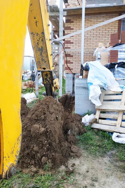 A escavadora cavando uma trincheira perto de uma casa de cabo para um pequeno balde . — Fotografia de Stock