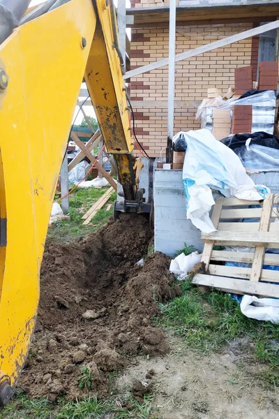 A escavadora cavando uma trincheira perto de uma casa de cabo para um pequeno balde . — Fotografia de Stock