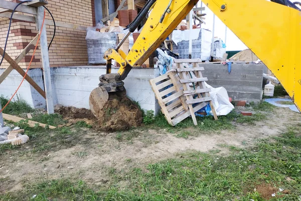 Koparka wykopuje dart wokół budynku, który jest w budowie. — Zdjęcie stockowe