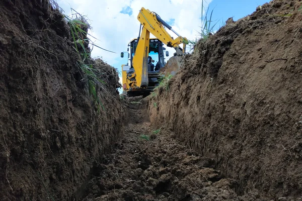 Sebuah ekskavator kuning menggali parit di lokasi konstruksi, close-up, terhadap langit . — Stok Foto