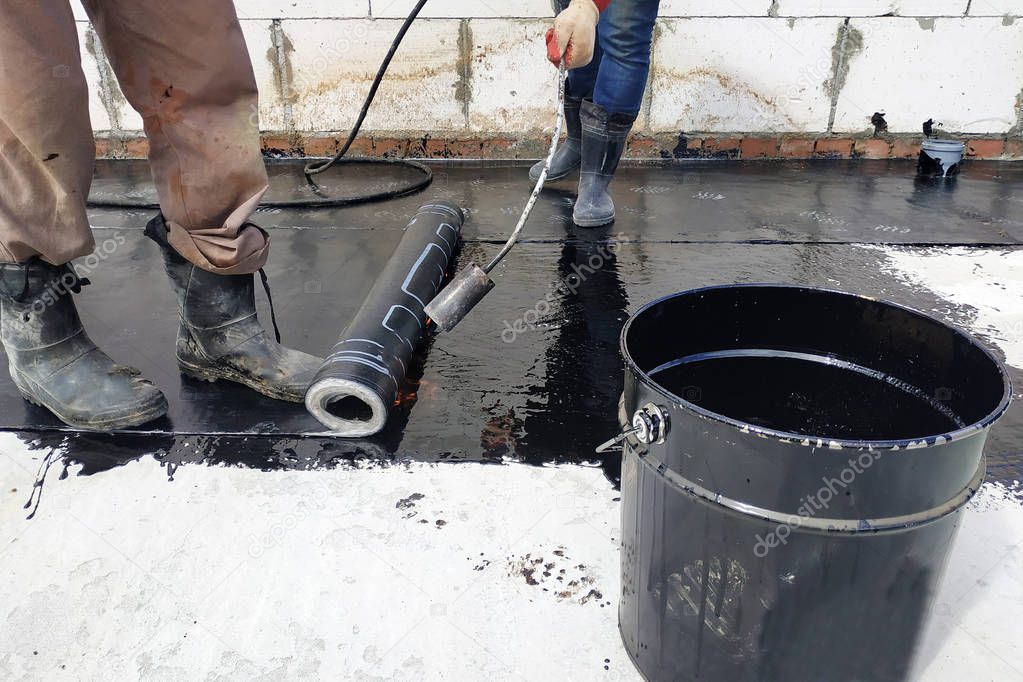 The workers cover the concrete screed with bituminous liquid solution and stele the waterproofing.