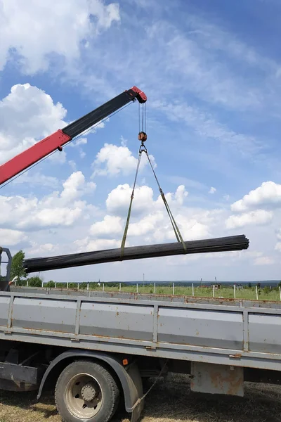 The truck crane in the field on the private land unloads the metal profile. — Stock Photo, Image