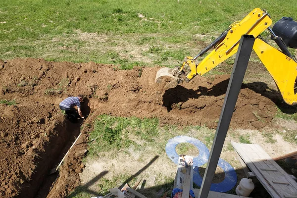 Ekskavatör eve elektrik kablosu döşemek için özel bir alanda bir siper kazır.