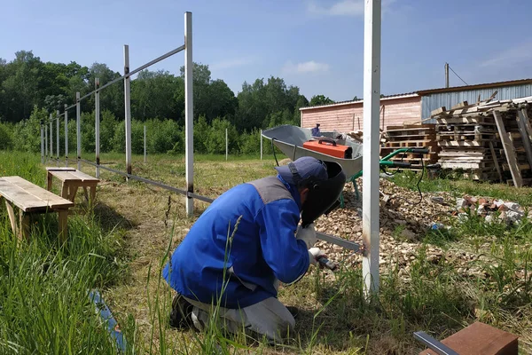 Ett staket installatör svetsar en metall profil till en ny staketstolpe. — Stockfoto