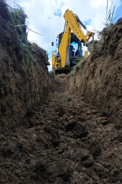 Una excavadora amarilla cavando una zanja en el sitio de construcción, un primer plano, contra el cielo . — Foto de Stock