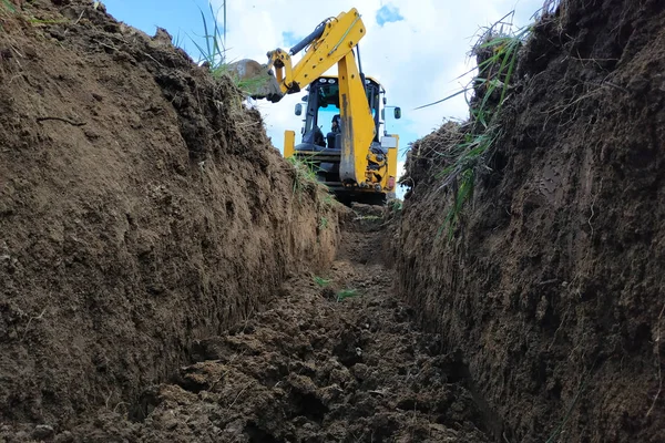 Sebuah ekskavator kuning menggali parit di lokasi konstruksi, close-up, terhadap langit . — Stok Foto