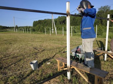 Koruyucu maske işçi kaynak çelik korkuluklar açık havada, kıvılcımlar gökyüzü ve alan arka plan karşı, aşağı sinek.