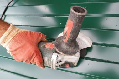 İşçi köyde açık havada bir açı öğütücü ile metal bir levha keser.