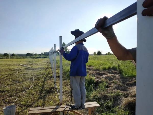 Trabalhador em máscara protetora solda corrimãos de aço ao ar livre, faíscas voam para baixo, contra o céu e fundo de campo . — Fotografia de Stock