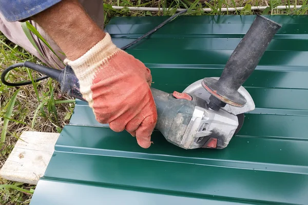 Çatı çalışmaları sırasında, bir inşaat işçisi bir açı öğütücü ile yamuk profili ile çelik bir levha spreyler.