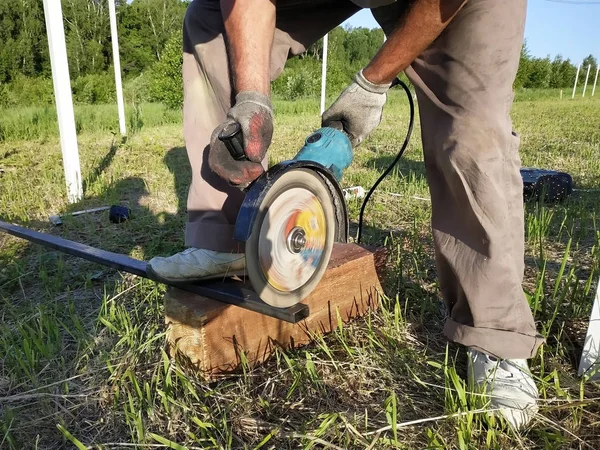 Un trabajador de amoladora angular corta un perfil metálico en el exterior . — Foto de Stock