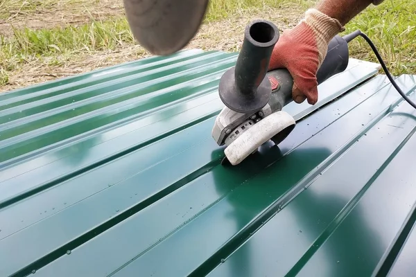 Durante o trabalho de cobertura, um trabalhador da construção pulveriza uma chapa de aço com um perfil trapezoidal com um moedor de ângulo . — Fotografia de Stock