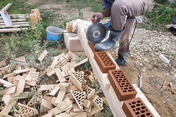 The worker cuts a corner brick with a front facade brick in the countryside.