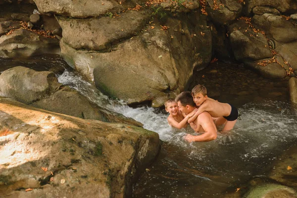 Um jovem pai e seus filhos tomam banho em um rio de montanha . — Fotografia de Stock