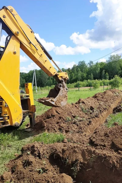 Un escavatore giallo scavare una trincea sul cantiere, un primo piano, contro il cielo . — Foto Stock