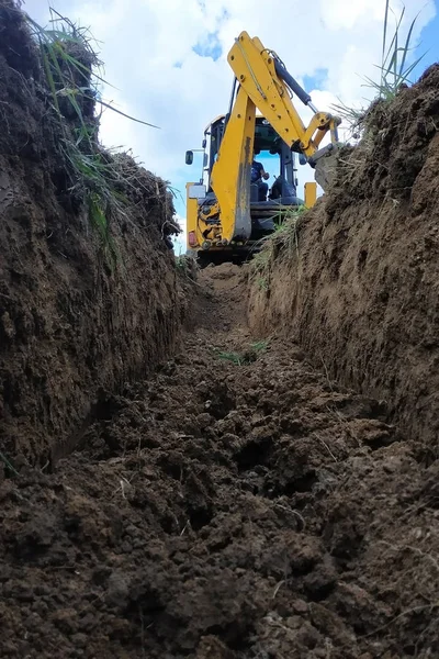 Un escavatore giallo scavare una trincea sul cantiere, un primo piano, contro il cielo . — Foto Stock