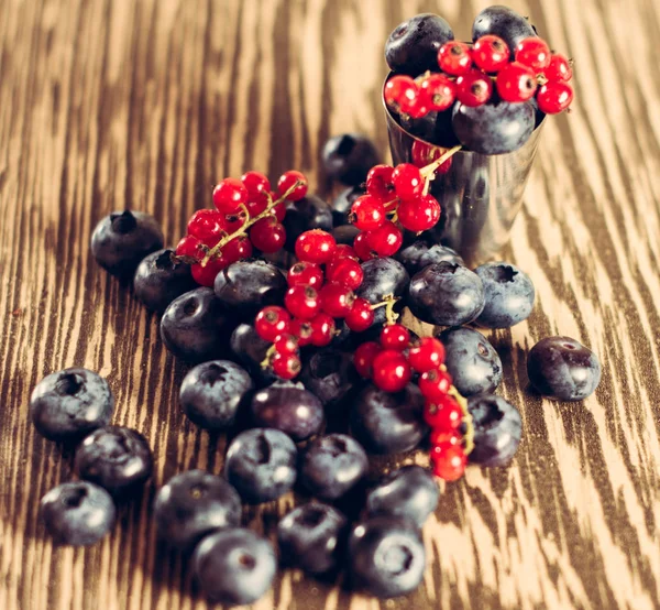 Glass with red currant and blueberries, brown background. — Stock Photo, Image