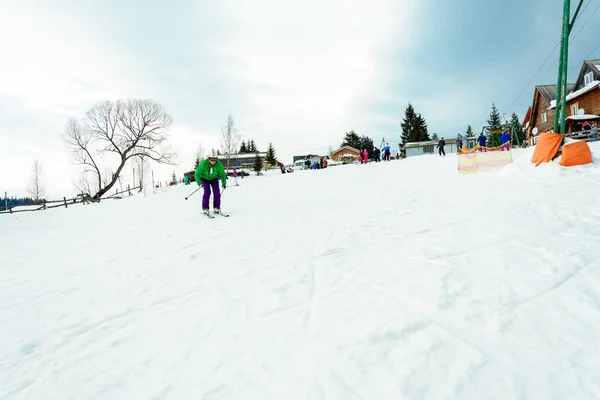 Yablunivka, ukraine februar 2019: Ein Mann in grüner Jacke geht im Karpatendorf auf dem Berg koryvka Skifahren. — Stockfoto