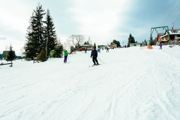 Yablunivka, ukraine februar 2019: Ein Mann in grüner Jacke mit Helm und Brille geht im Karpatendorf auf dem Berg Koryvka Skifahren. — Stockfoto