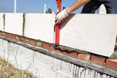 İşçi çalışma duvarını bir seviye ile ölçer.