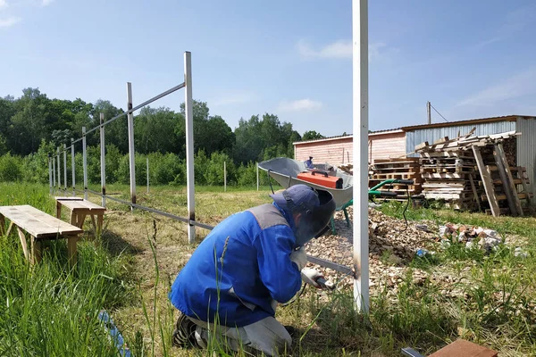 Na aldeia no canteiro de obras, um soldador solda uma cerca . — Fotografia de Stock