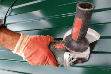 İşçi köyde açık havada bir açı öğütücü ile metal bir levha keser.