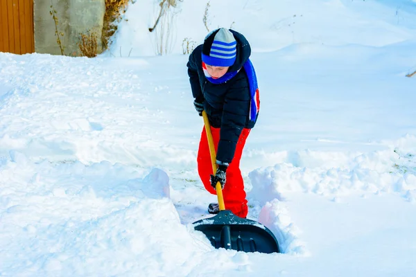 Um menino na aldeia limpa a neve e faz um passeio . — Fotografia de Stock