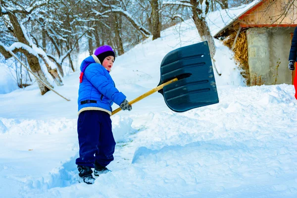 Depois de neve pesada, o menino limpa a neve com uma pá . — Fotografia de Stock