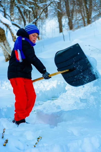 Limpiando nieve en invierno, el niño pala nieve . — Foto de Stock