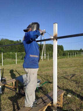 Koruyucu maske işçi kaynak çelik korkuluklar açık havada, kıvılcımlar gökyüzü ve alan arka plan karşı, aşağı sinek.