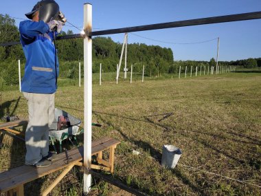 Koruyucu maske işçi kaynak çelik korkuluklar açık havada, kıvılcımlar gökyüzü ve alan arka plan karşı, aşağı sinek.